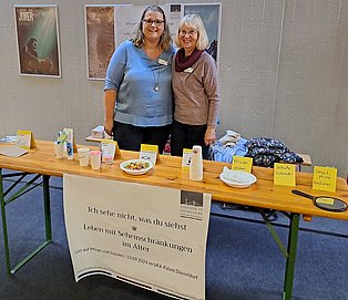 Zwei Frauen am Messestand zeigen auf einem Tisch Gegenstände